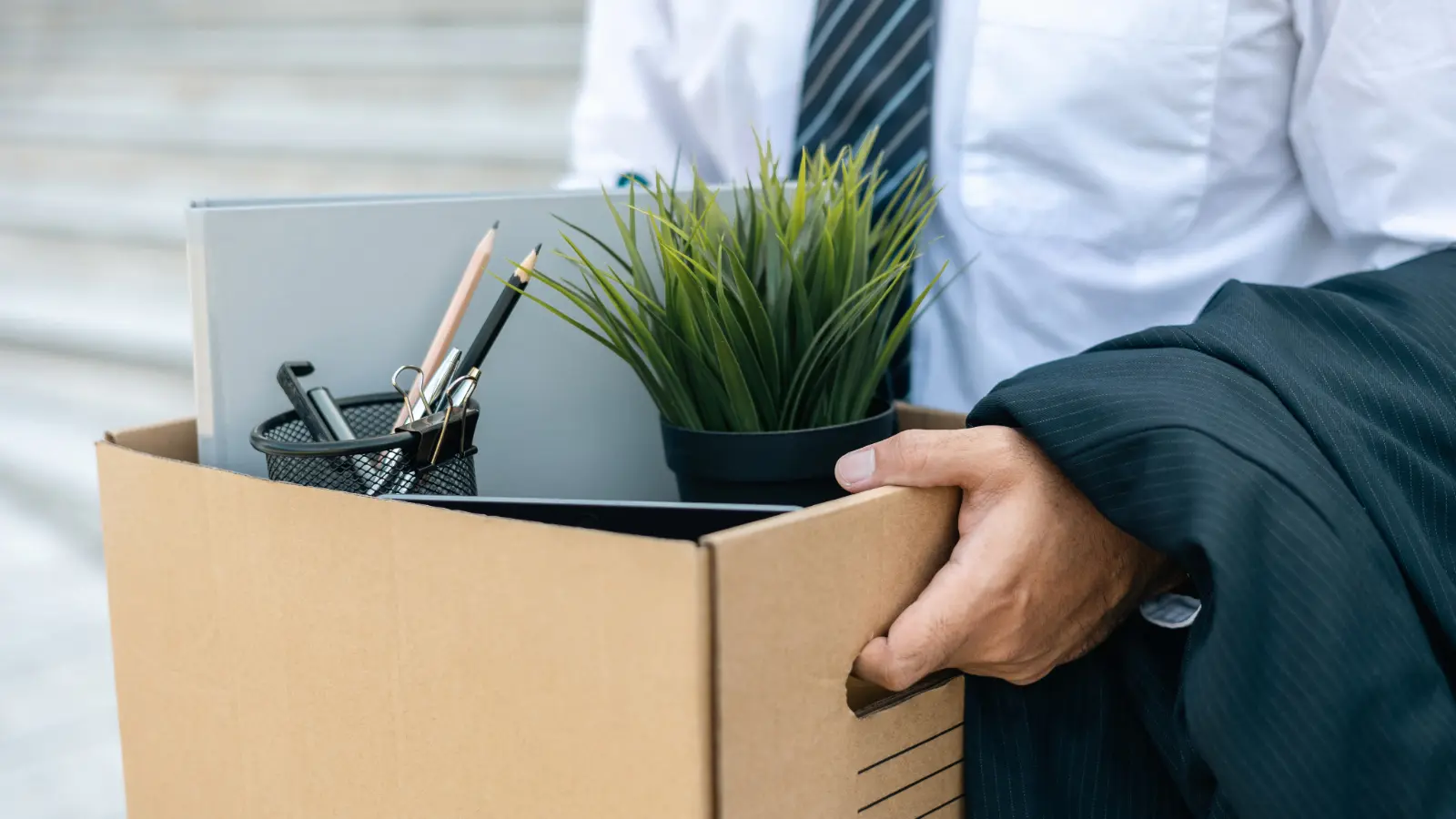 Close-up photo of a male executive holding a box of personal items from his desk, signifying that he has lost his job.